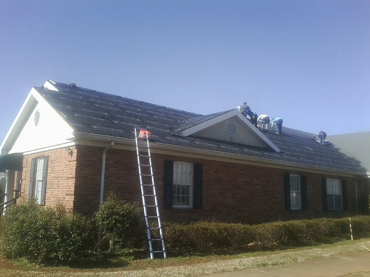 Crew tearing shingles off a brick ranch roof with a ladder set — Metal Roof Repair work by our crew in Bonnieville