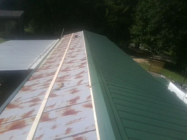 Old rusted panels beside newly installed green metal roofing — Wind Damage Roof Repair by Roofing Brothers in Bonnieville