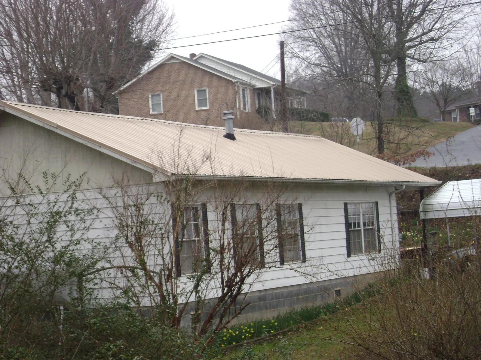 Tan metal roof on a white sided house set into a hillside — Commercial Roofing by Roofing Brothers in Bonnieville