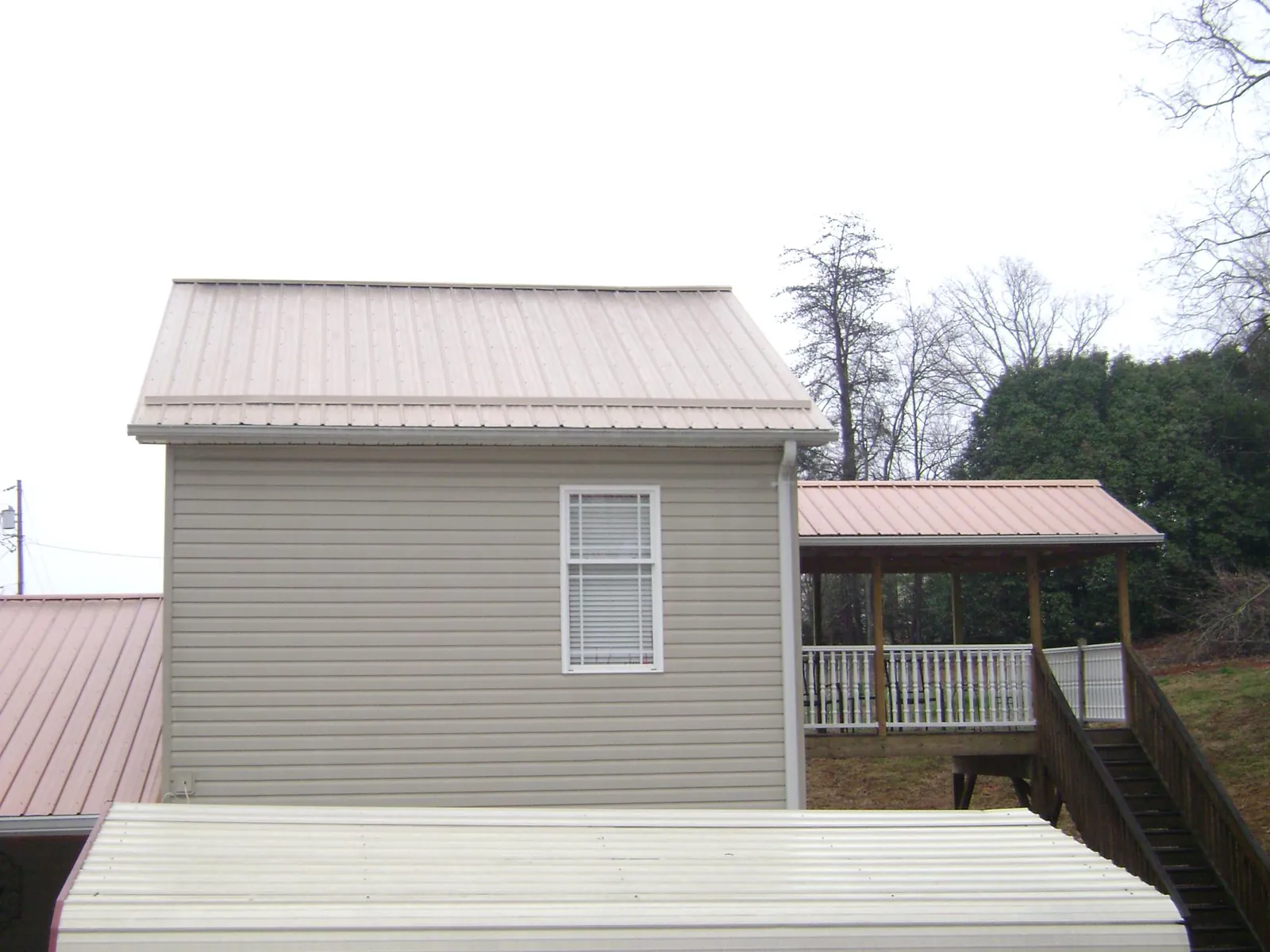 Tan metal roofs on a two story addition and attached porch, from a Roof Replacement job in Bonnieville